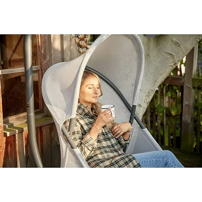 Siena Garden Hängesessel Yobaya mit Schutzhülle - L x B x H: 106 x 123 x 195 cm, Grau - Entspannte Frau genießt ihren Hängesessel mit integriertem Sonnenschutz und einer Tasse Kaffee für gemütliche Stunden im Garten.