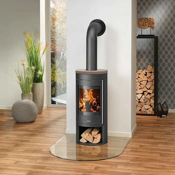Justus Kaminofen Mino 2.0 - 5,5 kW, Raumheizvermögen: 88 m³, Farbe Verkleidung: Grappa, Schwarz - Ein moderner Kaminofen mit Holzscheitlagerung und Glasplatte im Wohnzimmer.
