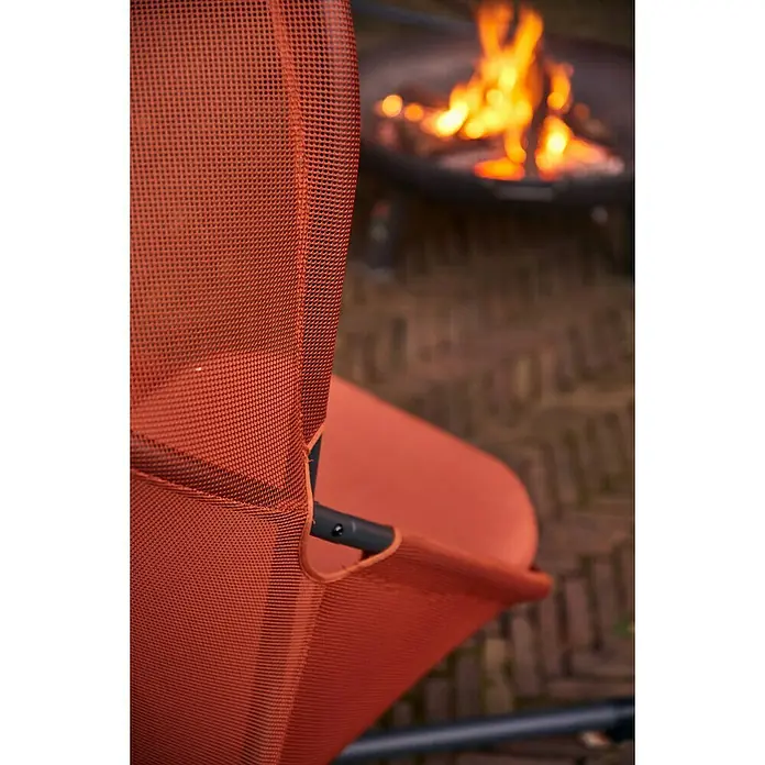 Siena Garden Hängesessel Yobaya mit Schutzhülle - L x B x H: 106 x 123 x 195 cm, Rot - Detailansicht eines orangefarbenen Outdoor-Stuhls aus Netzgewebe vor einem warmen Lagerfeuer. Der Stuhl lädt zum Entspannen ein.