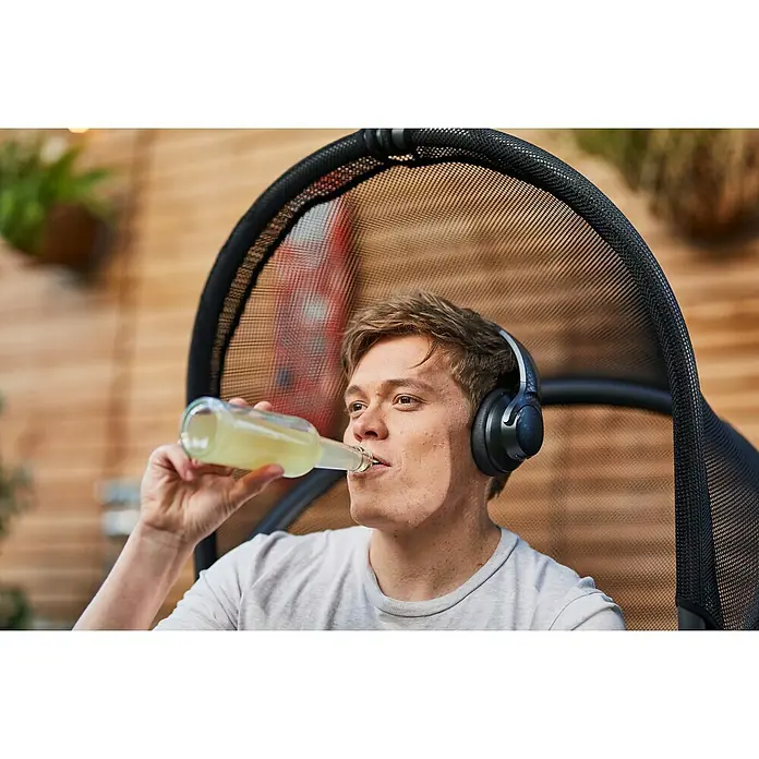 Siena Garden Hängesessel Yobaya mit Schutzhülle - L x B x H: 106 x 123 x 195 cm, Schwarz - Ein Mann sitzt mit Kopfhörern in einem Stuhl und trinkt aus einer Glasflasche. Die Kopfhörer sind gut sichtbar.