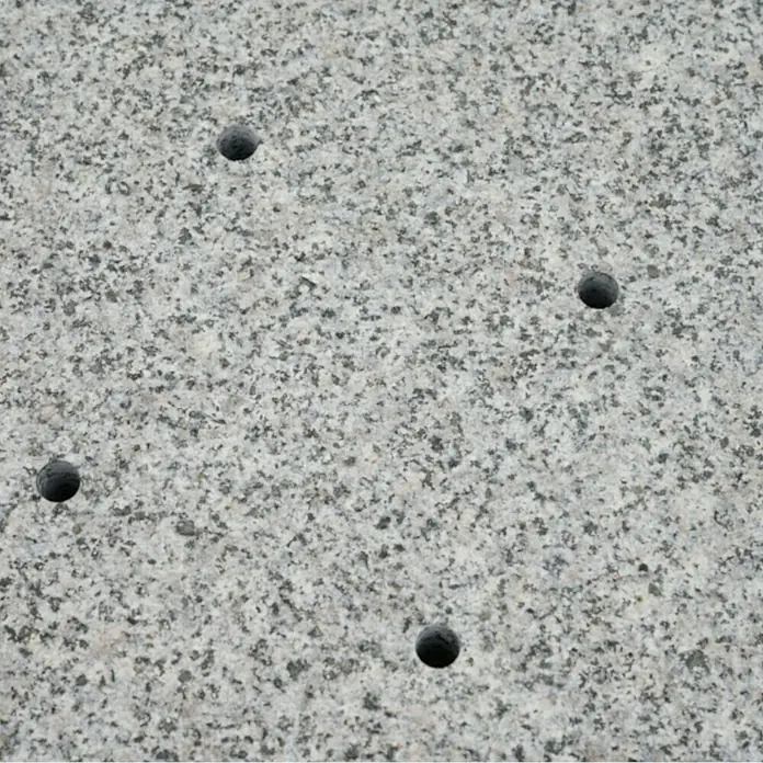 Siena Garden Granitschirmständer Ennio Base mit Rollen - 120 kg, L x B: 80 x 80 cm - Nahaufnahme einer polierten Granitplatte mit fünf runden Bohrlöchern. Der Stein hat ein gesprenkeltes Muster aus Grau- und Schwarztönen.