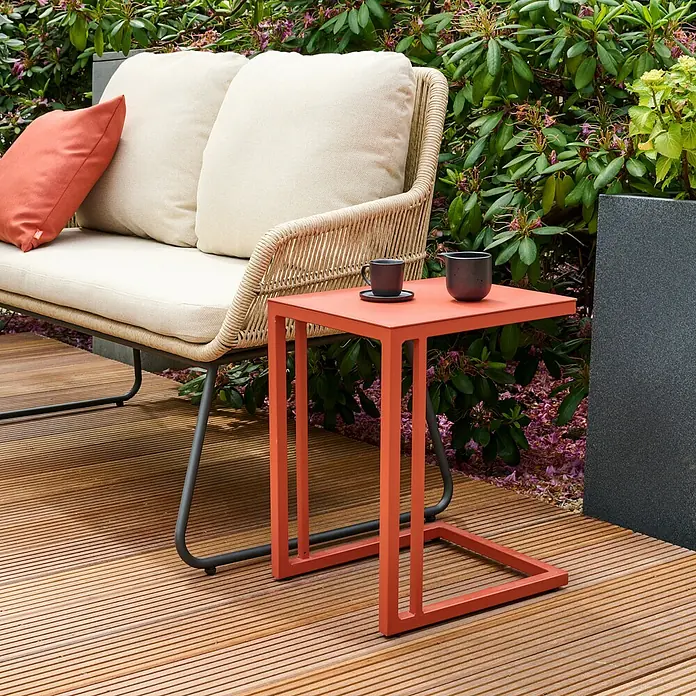 Siena Garden Garten-Beistelltisch Ramo - L x B x H: 33,5 x 40 x 50 cm, Aluminium, Quadratisch, Rot - Nahaufnahme eines orangefarbenen Beistelltisches mit Getränken auf einer Holzterrasse neben einem Outdoor-Sofa.