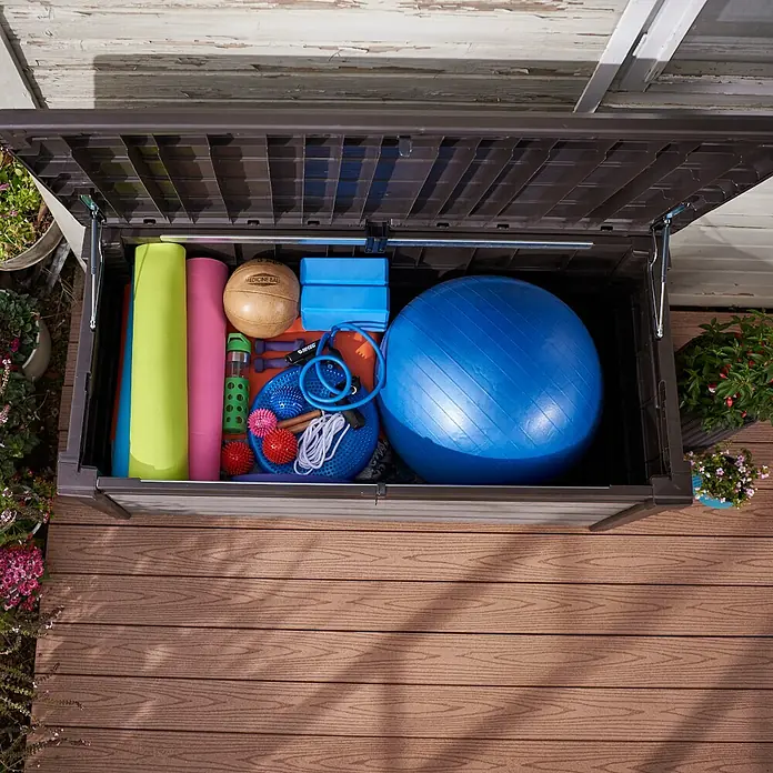 Siena Garden Garten-Aufbewahrungsbox Brushwood - 155 x 72,4 x 64,4 cm, Aluminium, Anthrazit (Holzoptik) - Eine braune Aufbewahrungsbox im Freien, voll mit Fitnessgeräten wie Yogamatten, Ball und Gewichten, ideal für die Lagerung im Garten.
