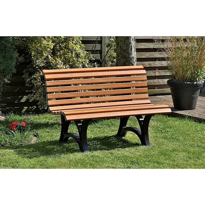 Blome Gartenbank Amrum - B x T x H: 120 x 64 x 80 cm, Holzoptik - Eine Gartenbank aus Holz mit schwarzen Beinen steht auf einem Rasen, neben einem Blumenbeet und einem Baumstamm.