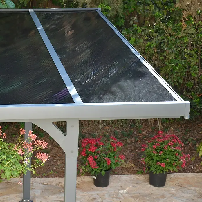 Palram – Canopia Carport Verona 5000 - Medidas ext. (An x Pr): 5,04 x 2,99 m, Aluminio, Carport adecuado para: Turismos - Primer plano de un moderno cenador de jardín gris con techo negro, rodeado de plantas florecientes. El cenador ofrece sombra y refugio en el jardín.
