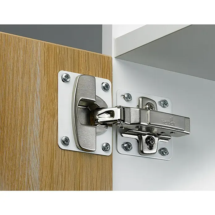 Hettich Montageplatte - L x B x H: 60 x 60 x 0,8 mm, Passend für: Topfscharnier Montageplatten - Verdecktes silbernes Möbelband an heller Holztür und weißem Korpus montiert.