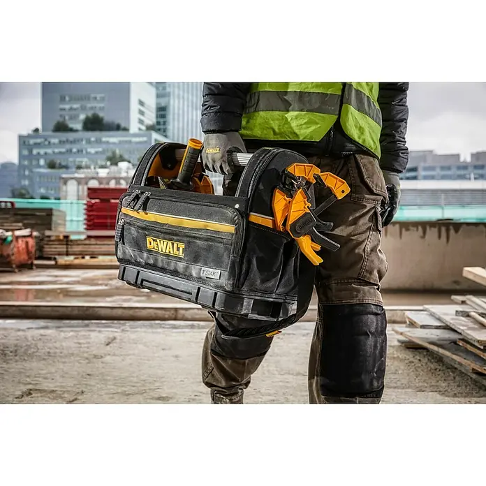 DeWalt T-STAK Werkzeugtasche - L x B x H: 25 x 45 x 35 cm, Textil, Traglast: 30 kg - Schwarze und gelbe DeWalt Werkzeugtasche mit gelben Zwingen, von einem Arbeiter auf einer Baustelle getragen.