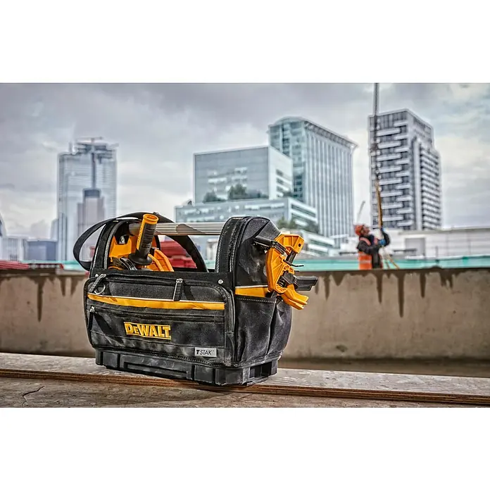 DeWalt T-STAK Werkzeugtasche - L x B x H: 25 x 45 x 35 cm, Textil, Traglast: 30 kg - Schwarze und gelbe DEWALT Werkzeugtasche gefüllt mit Werkzeugen, auf einer Baustelle mit Stadtgebäuden und einem Arbeiter im Hintergrund.