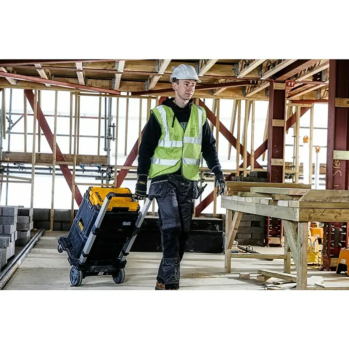 DeWalt T-STAK Portapapeles DWST82732-1 - L x An x Al: 28,5 x 41,3 x 32 cm, Plástico, Luz LED - Un trabajador arrastra una caja de herramientas rodante DeWalt negra y amarilla en una obra.