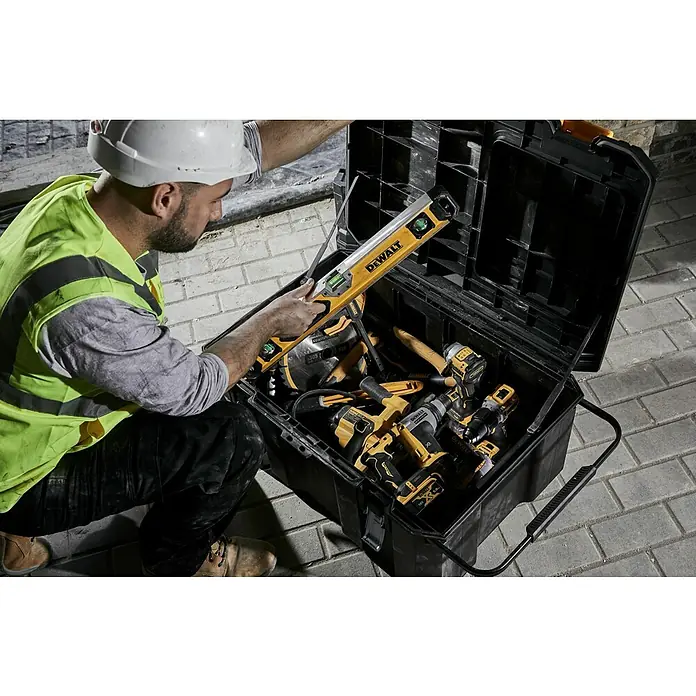 DeWalt T-STAK Werkzeugkasten - L x B x H: 80 x 60 x 43 cm, Kunststoff, Traglast: 50 kg - Ein Arbeiter mit Schutzhelm öffnet eine schwarze DeWalt Werkzeugkiste, die gelbe und schwarze DeWalt Elektrowerkzeuge wie Bohrer, Säge und Wasserwaage zeigt.