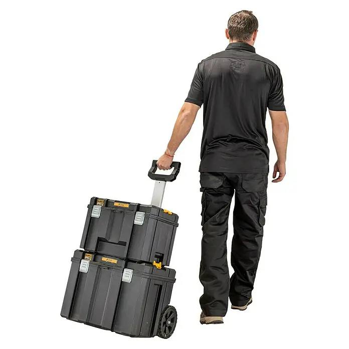 DeWalt T-STAK Aufbewahrungs- & Transportbox - L x B x H: 43,5 x 51,2 x 63,5 cm, Polypropylen, Traglast: 50 kg - Der Mann zieht einen Werkzeugwagen mit zwei DeWalt Werkzeugkisten. Der Werkzeugwagen ist schwarz und hat gelbe Akzente. Er steht auf zwei Rädern.