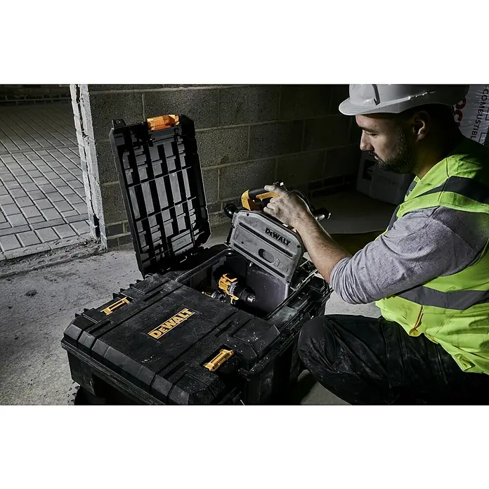DeWalt T-STAK Caja para herramientas - L x An x Al: 80 x 60 x 43 cm, Plástico, Capacidad de carga: 50 kg - Caja de herramientas DeWalt negra con detalles amarillos, abierta en una obra, con taladro, mientras un trabajador guarda una sierra circular.