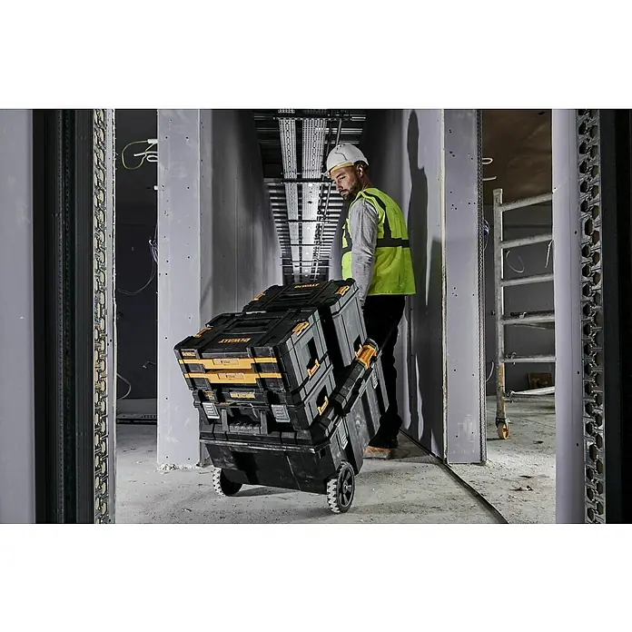 DeWalt T-STAK Werkzeugkasten - L x B x H: 80 x 60 x 43 cm, Kunststoff, Traglast: 50 kg - Stapelbare, schwarze und gelbe DeWALT TSTAK Werkzeugkisten auf Rollen, von einem Arbeiter auf einer Baustelle gezogen.