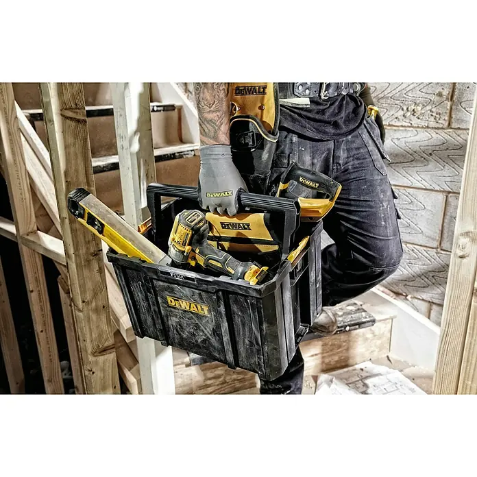 DeWalt T-STAK Werkzeugkasten - L x B x H: 44 x 32 x 27,5 cm, Kunststoff, Traglast: 50 kg - Schwarze DEWALT Werkzeugkiste mit gelben Akzenten, gefüllt mit Bohrmaschine und Wasserwaage, getragen von einer Person auf einer Baustelle.