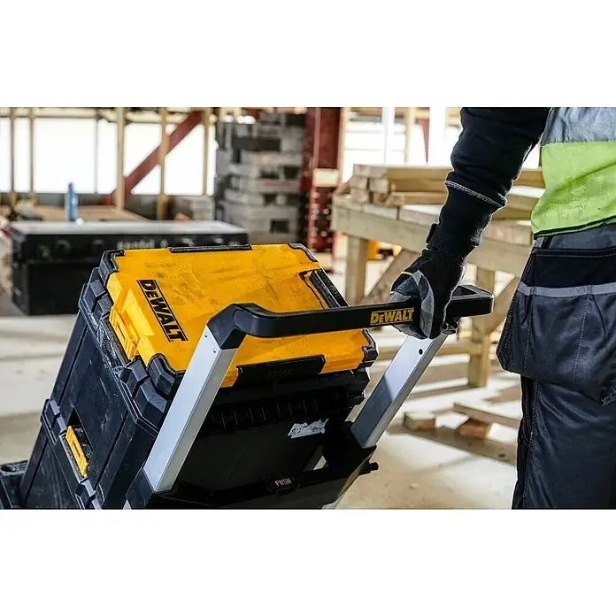 DeWalt T-STAK Portapapeles DWST82732-1 - L x An x Al: 28,5 x 41,3 x 32 cm, Plástico, Luz LED - Persona arrastrando un sistema de cajas de herramientas DeWalt apilables amarillo y negro en una obra.
