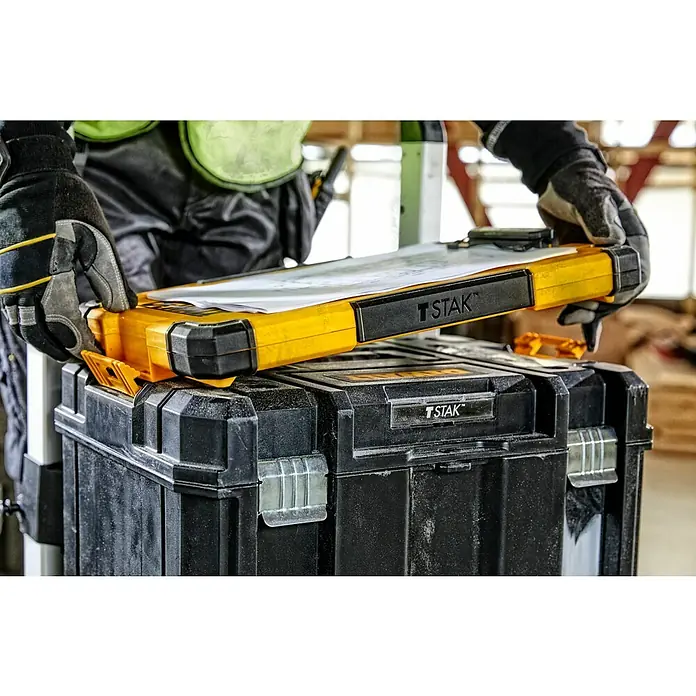 DeWalt T-STAK Portapapeles DWST82732-1 - L x An x Al: 28,5 x 41,3 x 32 cm, Plástico, Luz LED - Un trabajador con guantes coloca una caja de documentos amarilla T STAK con papeles sobre una caja de herramientas negra T STAK.
