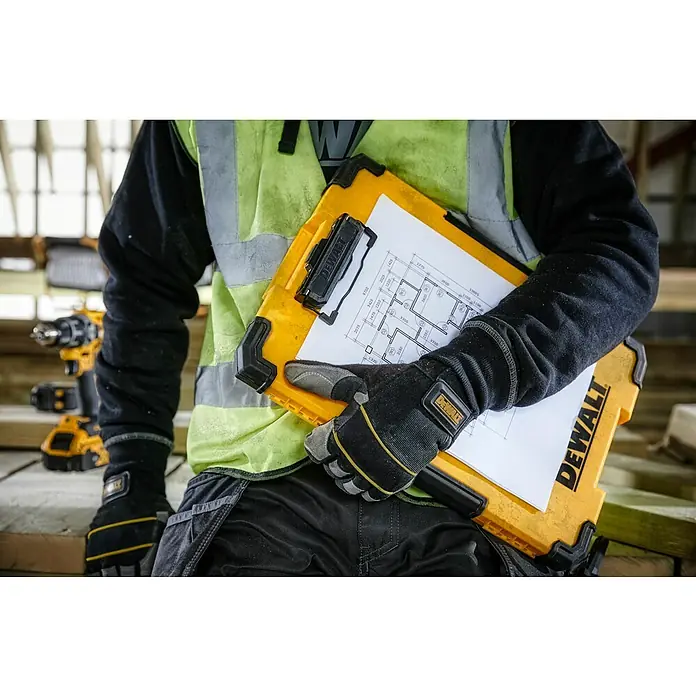 DeWalt T-STAK Klemmbrett - L x B x H: 28,5 x 41,3 x 32 cm, Kunststoff, LED-Licht - Nahaufnahme eines Mannes mit Dewalt-Arbeitshandschuhen, der ein gelbes Dewalt-Klemmbrett mit Bauplan hält.