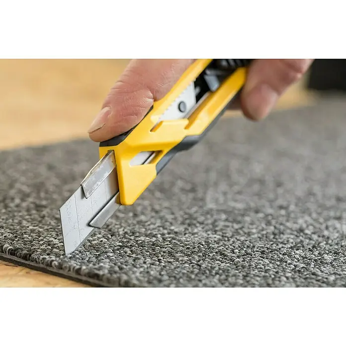 Stanley Cuttermesser Comfort Cut 18mm - Klingenbreite: 18 mm, Abbrechklinge - Nahaufnahme eines gelben Teppichmessers, das einen grauen Teppich schneidet und die Schärfe und Präzision des Werkzeugs hervorhebt.