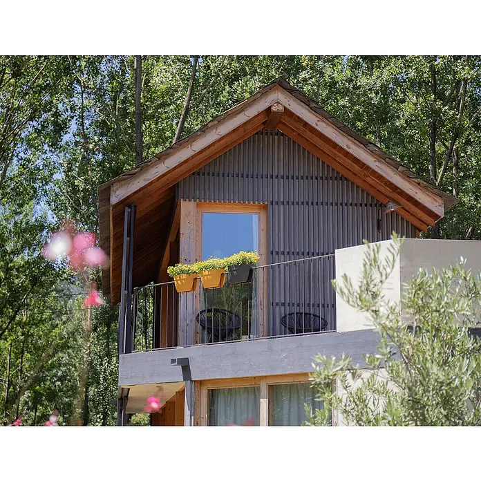 Artevasi Capri Campana Balkonkasten - L x B x H: 39 x 25,6 x 22,5 cm, Kunststoff, Grau, Matt - Das Foto zeigt ein modernes, zweistöckiges Gebäude mit Balkon, geschmückt mit Blumenkästen und umgeben von üppigem Grün.