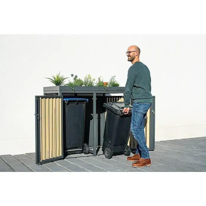Westmann Mülltonnenbox Planta - Stahl, Anthrazit/Braun, Geeignet für Anzahl Mülltonnen: 2 Stk. - Mann entsorgt Müll in einem WESTMANN Mülltonnenbox-System mit Bepflanzung auf der Oberseite.