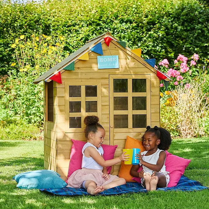 Zwerkules Spielhaus Holla - L x B x H: 97,5 x 121 x 140 cm, Holz, Natur - Zwei Mädchen spielen vor einem hellen Holzspielhaus mit bunten Girlanden und dem Schild "Home Sweet Home" im Garten.