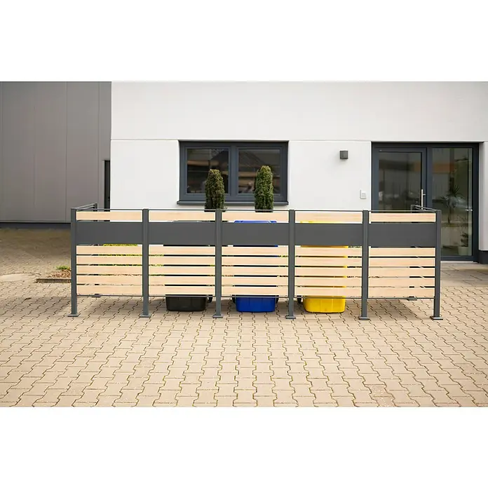 Westmann Mülltonnenbox Verkleidung Planum - 90 x 410 x 120 cm, Anthrazit/Holzoptik - Mülltonnenbox aus Holz und Metall vor einem modernen Gebäude, die Mülltonnen versteckt.