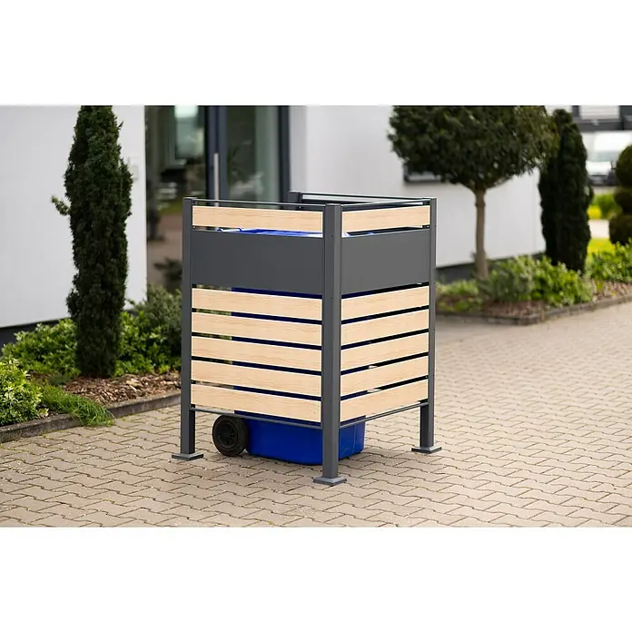 Westmann Mülltonnenbox Verkleidung Planum - 90 x 90 x 120 cm, Anthrazit/Holzoptik - Eine Mülltonnenbox mit einer Verkleidung aus hellen Holzlatten und grauen Metallrahmen, die eine blaue Mülltonne verdeckt, steht auf Pflastersteinen.