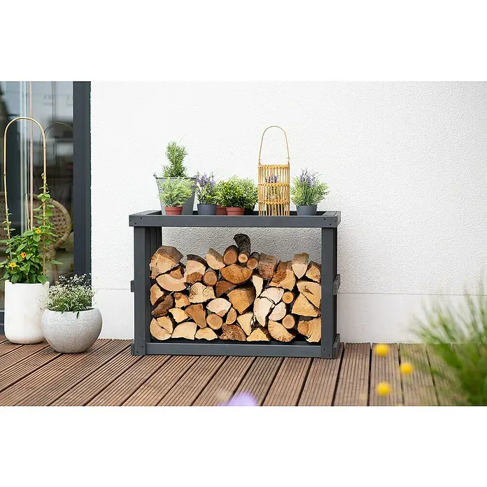 Westmann Kaminholzregal Stephan - 108 x 52 x 74 cm, Holz, Anthrazit - Ein graues Holzregal im Freien mit Brennholz gefüllt, dekoriert mit verschiedenen Pflanzen und einer Laterne.
