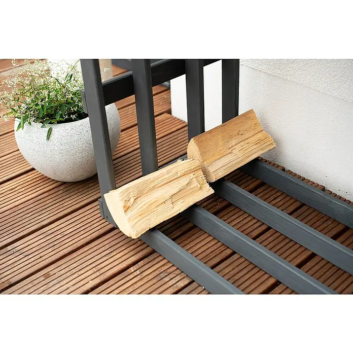 Westmann Kaminholzregal Stephan - 108 x 52 x 74 cm, Holz, Anthrazit - Holzscheite, die auf einem grauen Holzscheitregal im Freien gestapelt sind, neben einem dekorativen Topf mit grünen Pflanzen.