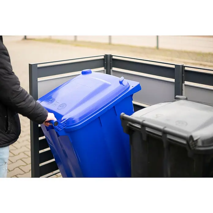 Westmann Mülltonnenbox Verkleidung Planum - 90 x 170 x 120 cm, Anthrazit/Grau - Blaue Mülltonne wird von einer Person vor einer grauen Mülltonne in einem Mülltonnenunterstand abgeholt.