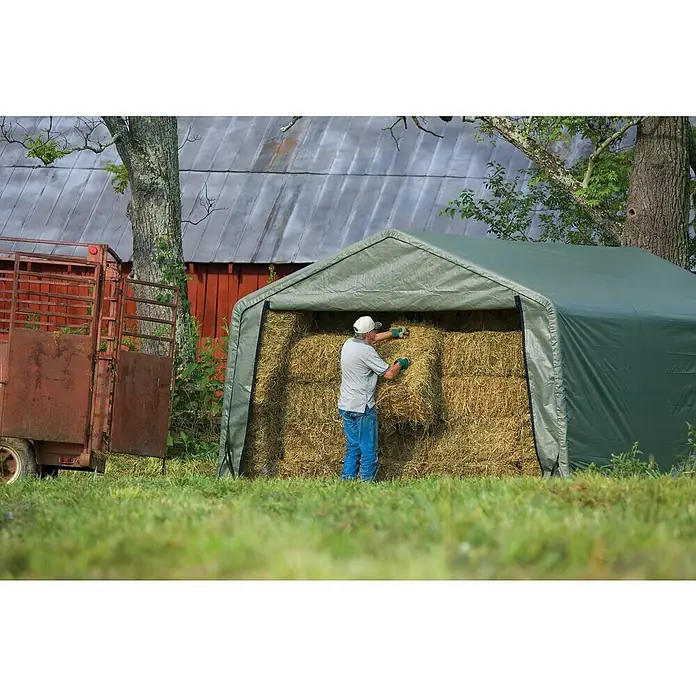 ShelterLogic Weidezelt - 610 x 380 cm, Kunststoff, Dunkelgrün - Grüner, tragbarer Unterstand zur Lagerung von Heuballen auf einem Bauernhof. Eine Person demonstriert darin die landwirtschaftliche Nutzung.