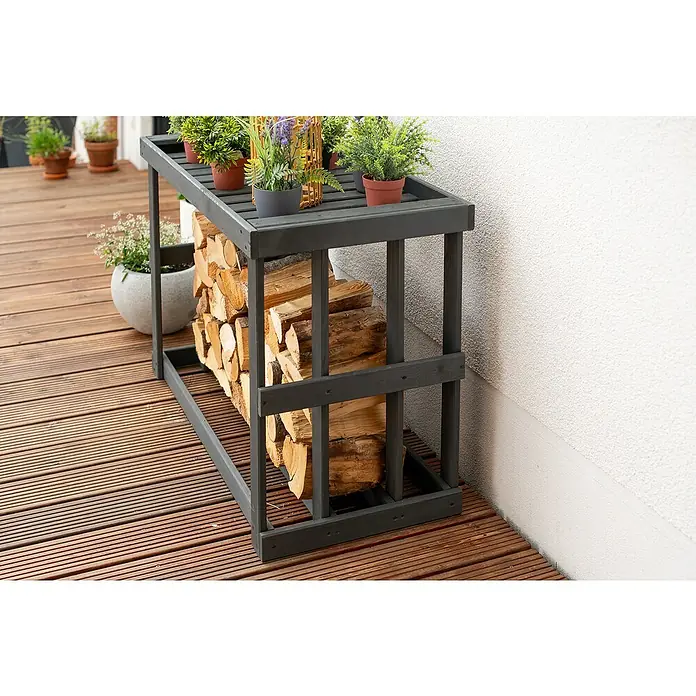 Westmann Kaminholzregal Stephan - 108 x 52 x 74 cm, Holz, Anthrazit - Brennholzregal aus dunklem Holz mit Pflanzen oben drauf, auf einer Terrasse.