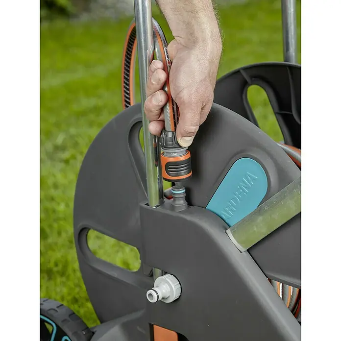 Gardena Schlauchwagen CleverRoll L Easy - Kunststoff/Metall, Schlauchkapazität: 100 m, 13 mm (½″) - Nahaufnahme einer Person, die einen Gartenschlauch an eine GARDENA Schlauchtrommel anschließt.