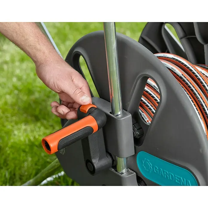 Gardena Schlauchwagen CleverRoll L Easy - Kunststoff/Metall, Schlauchkapazität: 100 m, 13 mm (½″) - Nahaufnahme einer Person, die eine Gardena Schlauchtrommel bedient, um den Gartenschlauch aufzurollen. Praktische Gartenbewässerung.