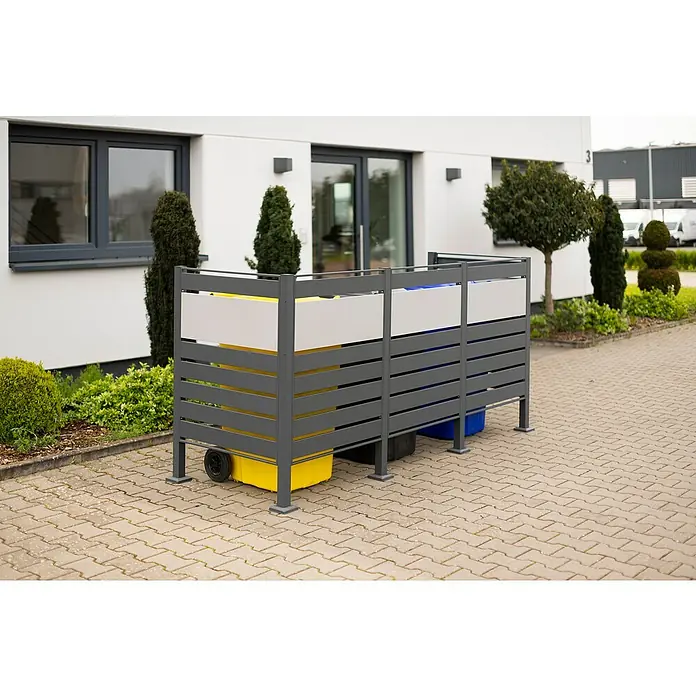 Westmann Mülltonnenbox Verkleidung Planum - 90 x 250 x 120 cm, Anthrazit/Grau - Hier ist ein Mülltonnenbox mit Lattenrost in Grau mit gelben und blauen Mülltonnen im Hof.