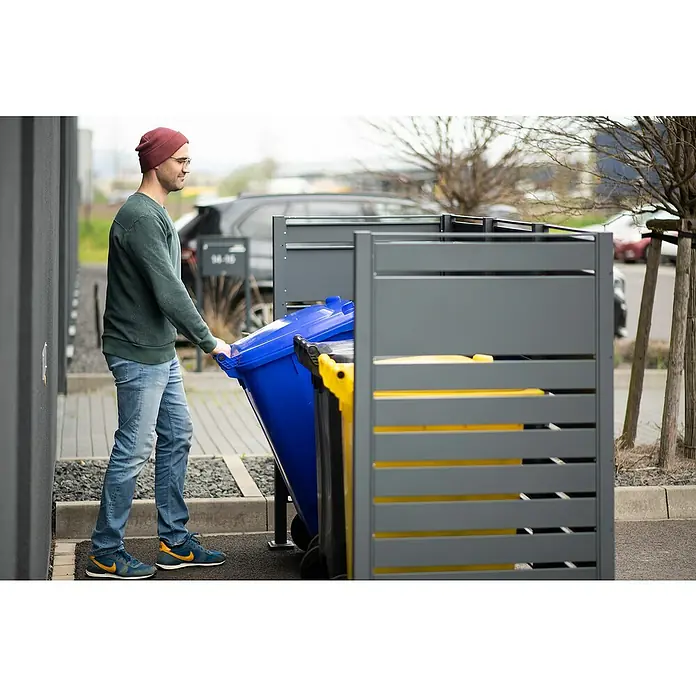 Westmann Mülltonnenbox Verkleidung Planum - 90 x 250 x 150 cm, Anthrazit - Mann schiebt eine blaue Mülltonne in eine graue Mülltonnenbox. Eine gelbe Tonne steht bereits in der Box.