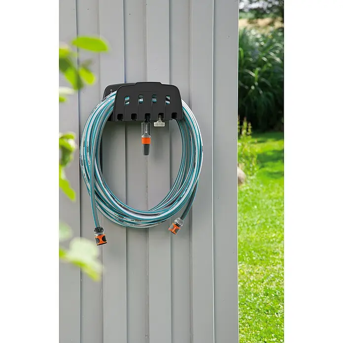 Gardena Classic Manguera para jardín - Largo: 20 m, Diámetro tubo flexible: 13 mm - Una unidad de almacenamiento de manguera de jardín Gardena con una manguera de jardín enrollada en una pared gris frente a un jardín verde.