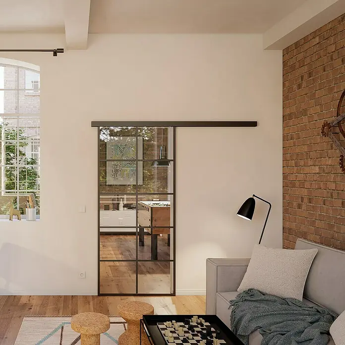 Room Plaza Slimwork Schiebetür-Komplettset Typ 8 - 940 x 2.060 mm, Klarglas - Schwarze Glasschiebetür mit Metallrahmen an einer Laufschiene, die zwei Räume in einem modernen Loft teilt.