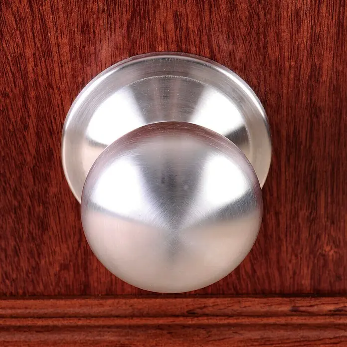 SegureStil Puerta de entrada interior S105 Serie V - 90 x 206 cm, Derecha, Sapelly, Acorazada - Primer plano de un pomo de puerta redondo plateado sobre una puerta de madera. El pomo está bien hecho y refleja la luz.