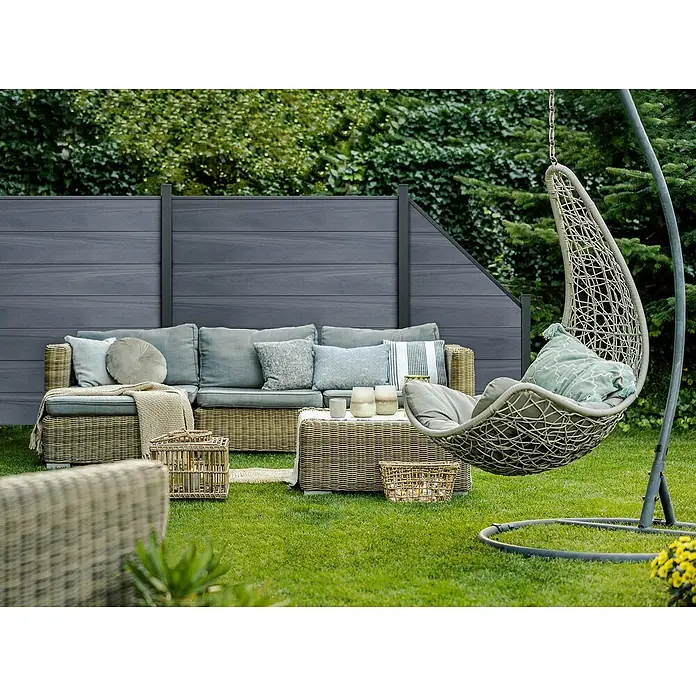 GroJa Solid Steckzaun Grande - 180 x 180 cm, Steingrau - Geflochtene Outdoor-Ecksofa mit grauen Kissen und passendem Hängesessel in einem Garten.