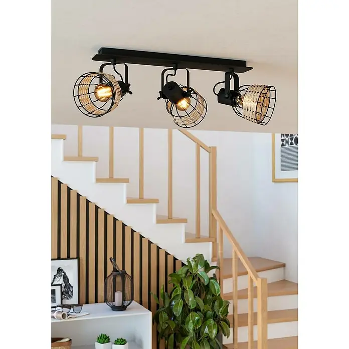 Eglo Anwick Deckenstrahler - 120 W, L x B x H: 67 x 14 x 24 cm, 3 Stk. - Eine Deckenleuchte mit drei Strahlern mit Lampenschirmen aus schwarzem Metalldraht und Rattan vor einem Treppenhaus.