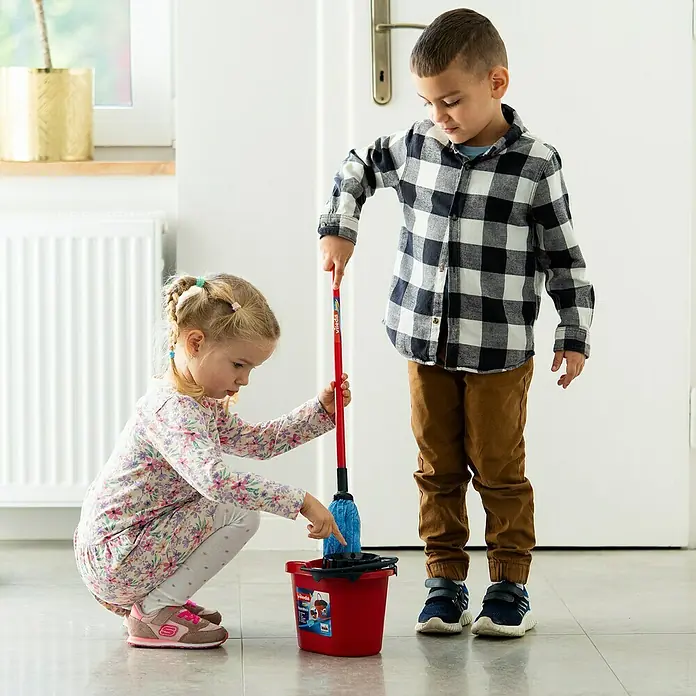 Klein Vileda Kinder-Wischmop-Set - 2 -tlg. - Zwei Kinder, ein Junge und ein Mädchen, spielen mit einem roten Vileda-Eimerset und einem blauen Wischmopp.