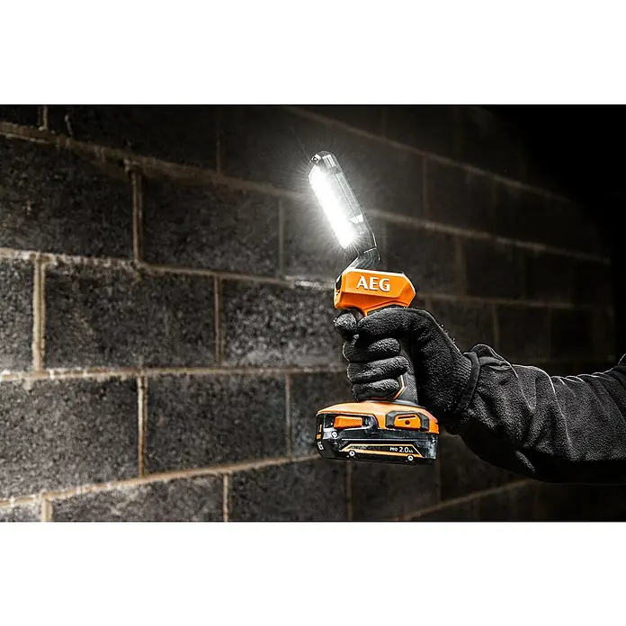 AEG Pro 18V LED-Akkustrahler BSL 18 - 18 V, Ohne Akku, 800 lm - Behandschuhte Hand hält eine beleuchtete orange-schwarze AEG Akkulampe vor dunkler Wand.