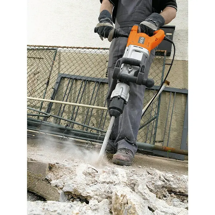 AEG Abbruchhammer PM 10E - 1.600 W, 20 J, SDS-Max-Aufnahme - Person benutzt einen orange-silbernen AEG Bohrhammer zum Zerkleinern von Beton, dabei entsteht Staub.