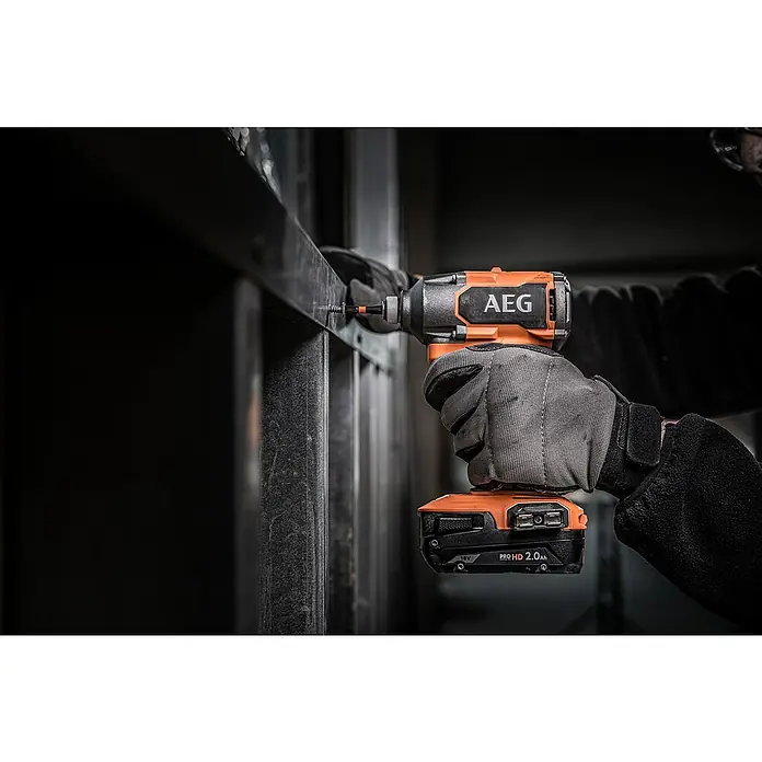 AEG Pro 18V Akku-Schlagschrauber Kompakt BSS 18C3B3 - 18 V, Ohne Akku, 350 Nm - Nahaufnahme einer behandschuhten Hand, die einen orange-schwarzen AEG Schlagschrauber hält und eine Schraube in einen Metallrahmen dreht.
