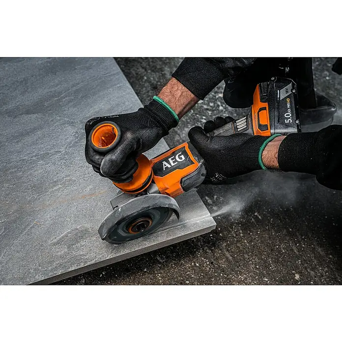 AEG Pro 18V Akku-Winkelschleifer BEWS 18-125BLPX2 - 18 V, Ohne Akku, Durchmesser Scheibe: 125 mm - Person in Handschuhen schneidet mit orange-schwarzem Akku-Winkelschleifer eine graue Fliese, Staub entsteht.