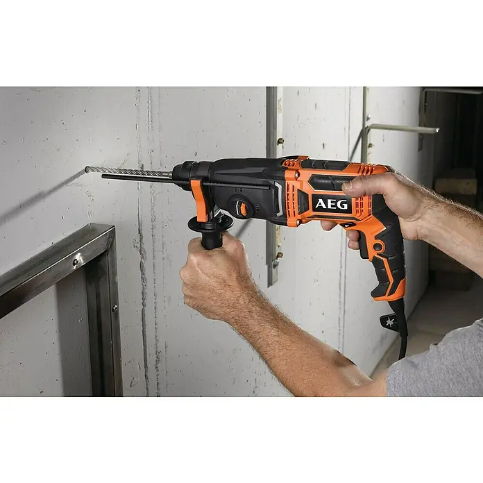 AEG Bohrhammer BH 24IE - 800 W, 2,4 J, Schnellspannbohrfutter - Orange-schwarzer AEG Bohrhammer wird von einer Person zum Bohren in eine Betonwand verwendet.