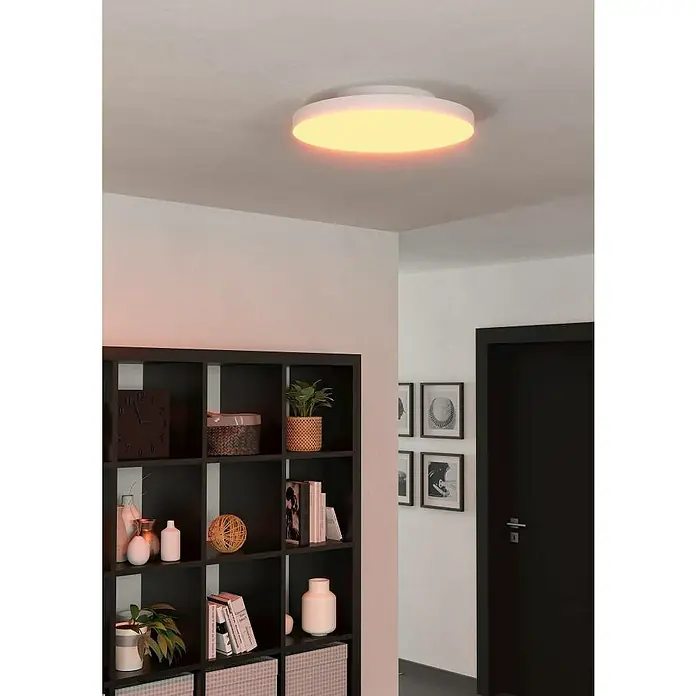 Eglo LED-Panel Turcona-Z - 22,4 W, L x B x H: 45 x 45 x 7,5 cm, Weiß, RGB - Eine moderne, runde Deckenleuchte mit warmem Licht erhellt einen Flur mit Regal und Tür. Das Leuchtmittel sorgt für eine angenehme Atmosphäre.