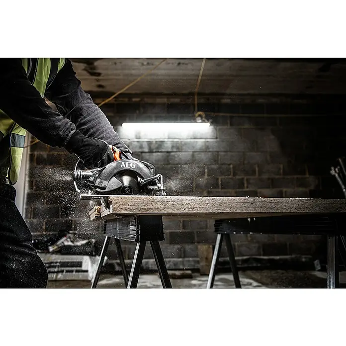 AEG Pro 18V Akku-Handkreissäge BKS 18BL2 - 18 V, Ohne Akku, 0 U/min - 5.400 U/min - Eine Person in Handschuhen schneidet ein Holzbrett mit einer AEG-Kreissäge, wodurch Sägespäne entstehen.