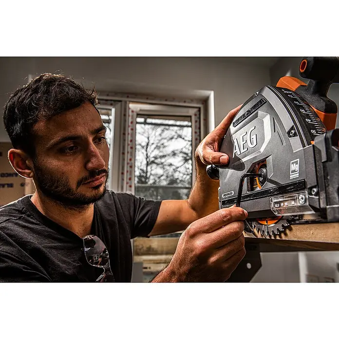 AEG Pro 18V Akku-Tauchsäge BKS 18PBL - 18 V, Ohne Akku, Durchmesser Sägeblatt: 165 mm, 0 U/min - 5.000 U/min - Mann stellt eine grau-orange AEG Handkreissäge mit Inbusschlüssel ein, um Holz zu schneiden.